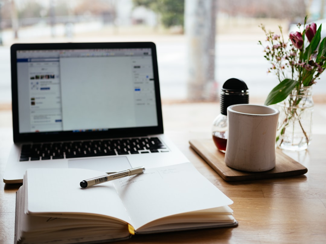 Person writing in a notebook surrounded by books and a laptop